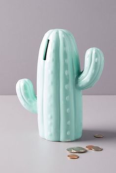 a green cactus shaped money bank sitting on top of a table next to some coins