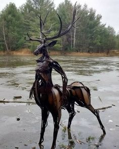 two metal deer sculptures sitting on top of ice covered ground next to trees and water