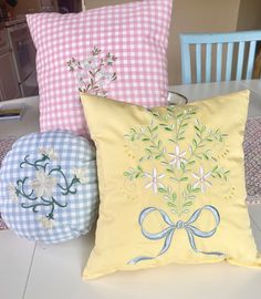 three decorative pillows sitting on top of a white table next to a blue and pink chair