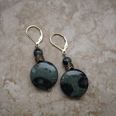 These green stone earrings are made with Kambaba stone. Kambaba is two shades of green, and each pattern is unique. You will love wearing these brilliant green lever-back earrings. *Kambaba coin-shaped stone: measures .7 inch in diameter *Accents: Gold-plated beads and a small, round Kambaba stone *14k gold-filled lever backs *Approximate length of earrings: 2 inches Bohemian Round Jade Earrings, Green Round Earrings, Green Jade Earrings With Natural Stones, Nickel-free Green Round Earrings, Nickel Free Round Green Earrings, Green Nickel-free Round Earrings, Green Natural Stones Drop Earrings, Green Natural Stone Drop Earrings, Green Brass Earrings With Natural Stones