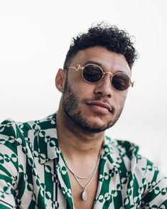 a man wearing sunglasses and a green striped shirt looks at the camera with his hand on his chest