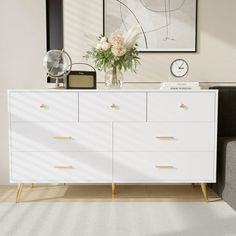 a white dresser sitting next to a couch in a living room with pictures on the wall