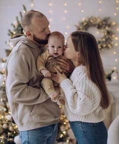 a man and woman holding a baby in front of a christmas tree