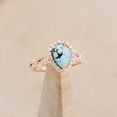 a turquoise and white stone ring on top of a wooden stand with diamonds around it