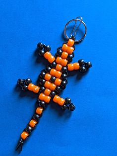 an orange and black beaded cross on a blue surface with a metal ring hanging from it's side