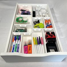 an organized drawer filled with pens, markers and other office supplies on a white surface