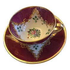 a cup and saucer sitting on top of a red plate with gold trimmings