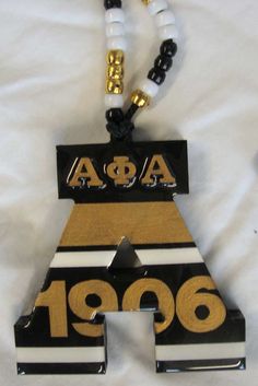 a black, white and gold necklace with an aca logo on the front hanging from a beaded cord