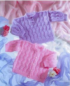 two knitted sweaters laying next to each other on top of blue and pink fabric