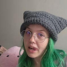 a woman with green hair wearing glasses and a knitted hat is making a funny face