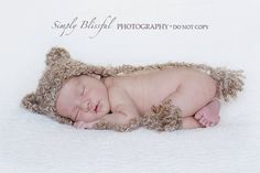 a newborn baby is sleeping in a brown teddy bear hat on a white blanket with his eyes closed