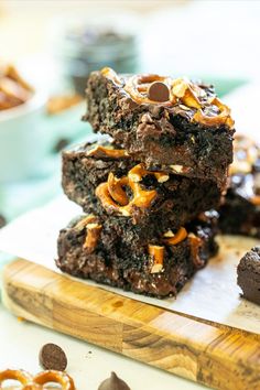 three chocolate brownies stacked on top of each other with pretzels in the background