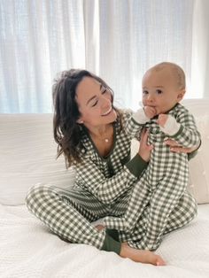 a woman holding a baby in her arms on top of a white bed and smiling