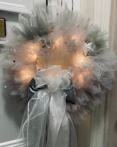 a white wreath with lights on it hanging from the front door, decorated with tulle