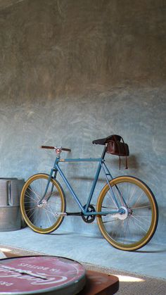 a blue bicycle parked against a wall next to two beer cans and a can opener