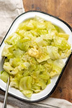 a white bowl filled with cabbage and some seasoning on top of the salad is sitting on a wooden table