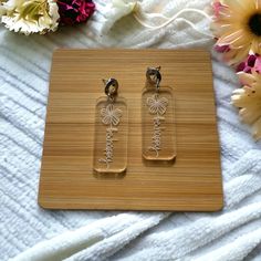 two clear glass earrings sitting on top of a wooden cutting board next to some flowers