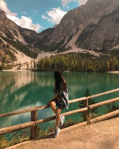 a woman is sitting on a fence looking at the water and mountains in the distance