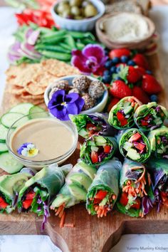 a wooden cutting board topped with lots of veggies and fruit next to dipping sauce