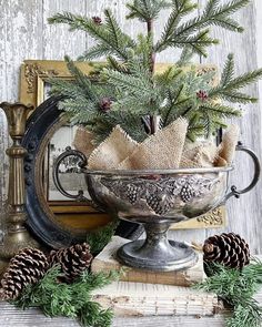 a metal bowl filled with pine cones and greenery on top of a wooden table