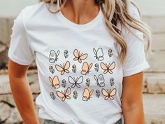 This Butterfly Flower t-shirt features delicate, soft, line art of butterflies and flowers, creating a beautiful and elegant design. Perfect for nature and gardening lovers, this tee is ideal for adding a subtle, artistic flair to any casual look. Our cute comfy Tee is crafted from soft, midweight cotton, offers versatility for effortless layering or standalone wear in the warmer months. Combining style and comfort seamlessly, we believe this tee encompasses all your wardrobe needs. Our T-shirt is designed in UNISEX style, offering a relaxed fit that runs true to size. If you want an oversized look, size up, consider sizing down for a snug fit.   We prioritize comfort and quality... - Crafted from lightweight and breathable material, weighing just 4.2 oz/yd² (142 g/m making it ideal for su White Butterfly T-shirt For Summer, Feminine Relaxed Fit T-shirt For Spring, White Butterfly T-shirt For Spring, White Butterfly-shaped Top For Summer, Butterfly Print Short Sleeve Tops For Spring, Feminine White T-shirt For Spring, Short Sleeve Tops With Butterfly Print For Spring, White Floral Print Feminine Shirt, Casual Butterfly Print Shirt For Spring