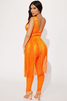 a woman wearing an orange jumpsuit with fringes on the sides and one leg