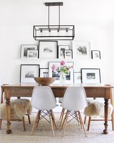 a dining room table with white chairs and pictures on the wall above it, along with framed photos