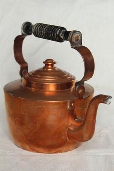 an old copper tea kettle with a black handle on a white tableclothed background