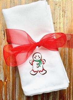 a white napkin with a red ribbon around it and a small embroidered snowman on the front