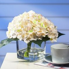 a vase with white flowers on a table next to a coffee cup and saucer