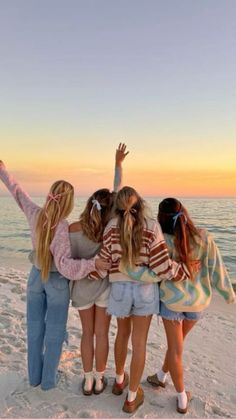 four girls standing on the beach with their arms in the air