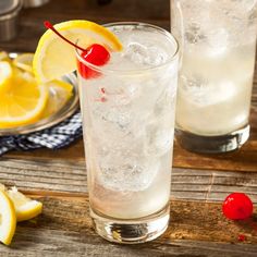 two glasses filled with lemonade and cherries on top of a wooden table next to sliced