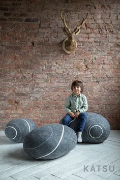 a young boy sitting on top of two large balls in front of a brick wall