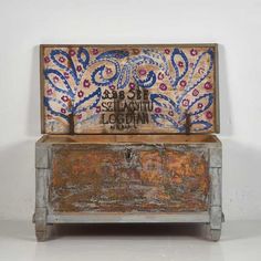 an old wooden box with painted designs on it's lid and bottom, sitting against a white wall