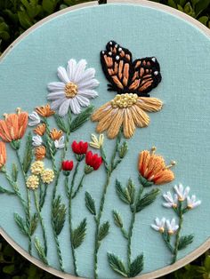 two butterflies sitting on top of flowers in a embroidery hoop with green grass behind it