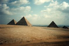 three pyramids in the desert under a cloudy sky