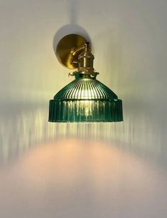 a green glass light hanging from the side of a white wall in a corner room