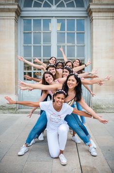 a group of young women posing for a photo in front of a building with their hands up