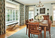 a dinning room table and chairs in front of two windows with drapes on them