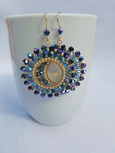 a close up of a pair of earrings on a white cup with blue and gold beads