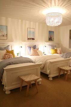 two twin beds in a bedroom with white walls and carpeted flooring, one has a chandelier above the bed