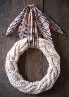 a knitted wreath with an origami bow hanging from it on a wooden surface