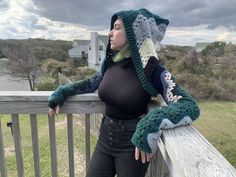 a woman wearing a crocheted hat and scarf on top of a wooden fence