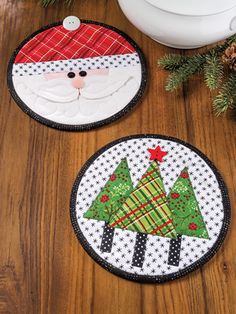 two christmas coasters sitting on top of a wooden table next to a pot holder