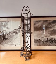 a metal fish sculpture sitting on top of a wooden table next to two framed pictures