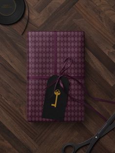 a gift wrapped in purple and black paper with a gold key on it next to a pair of scissors