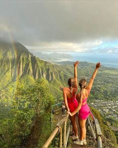 two women standing on the top of a mountain with their arms up in the air