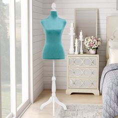 a mannequin is standing next to a bed in a room with white walls