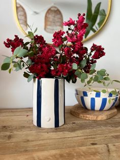 red flowers sit in a striped vase next to a blue and white bowl on a wooden table