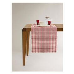 a red and white checkered table cloth with two cups on it, sitting at a wooden table